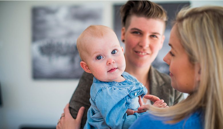 A woman holding a baby and another woman looking on.