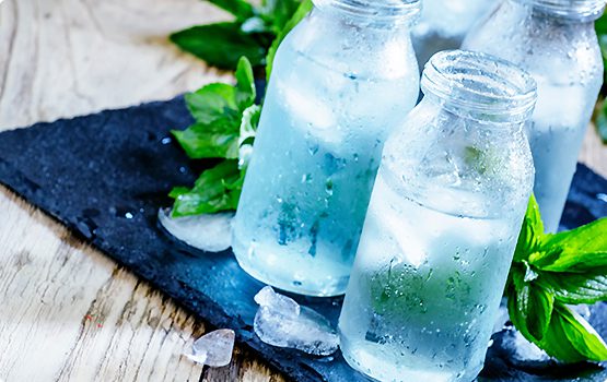 Two bottles of water with ice on a table.